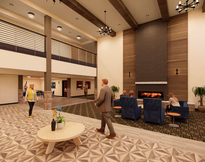 A spacious senior living facility common area with high ceilings and modern decor. Several people are present, some walking and others seated in blue armchairs around a large fireplace. The floor has a patterned design, and there is a round wooden table with plants in the foreground. The upper level has a railing overlooking the area.