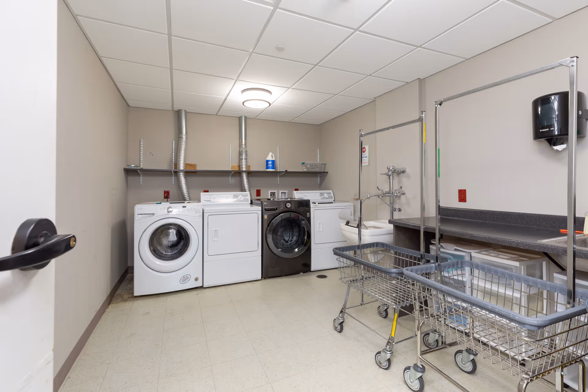 Interior laundry room with washers and dryers, laundry carts, folding counter and utility sink.