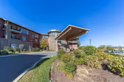 Exterior view of a multi-story senior living facility named The Summit with a covered entrance, landscaped bushes, and a driveway under a clear blue sky.