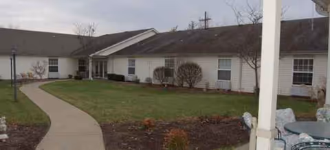 Single-story senior living facility exterior with a curved walkway and surrounding lawn.