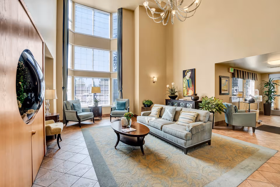 Bright, spacious lobby/lounge with tall windows, a sofa and armchairs arranged around a coffee table and decorative plants.