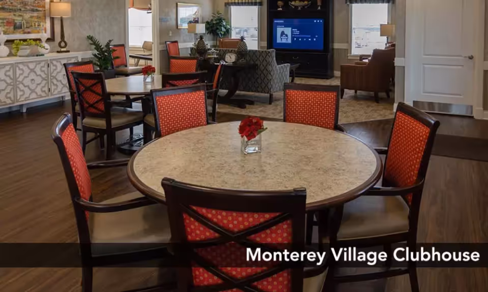 Clubhouse dining area with round tables, red-upholstered chairs, and a TV in the background.