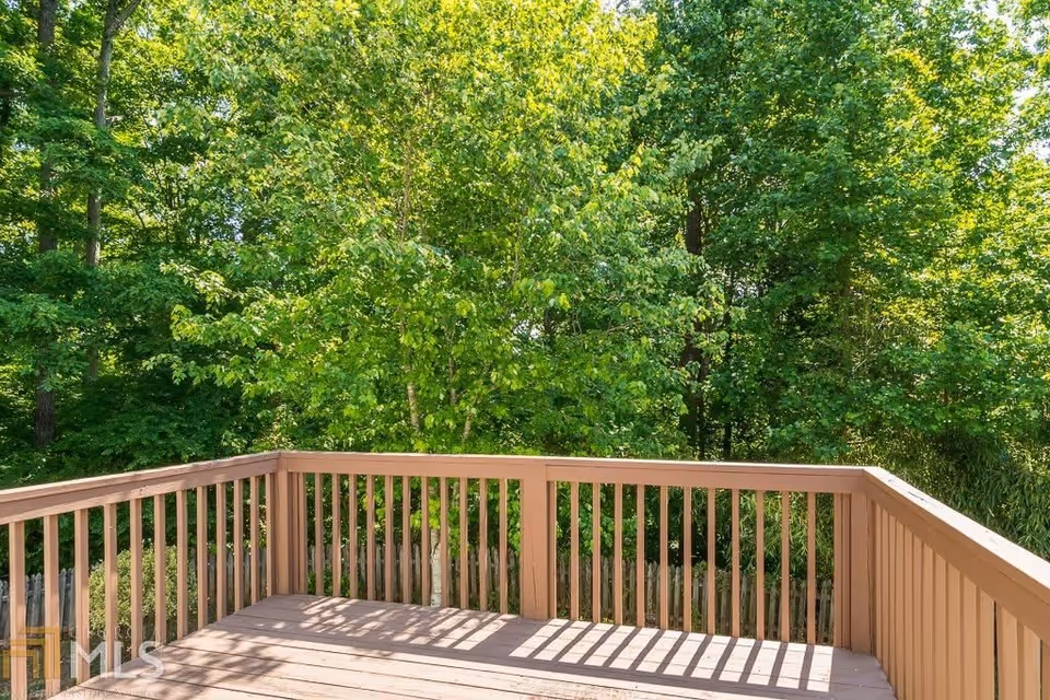 A wooden deck railing with vertical slats overlooking a lush green forest with dense trees and foliage under bright daylight.