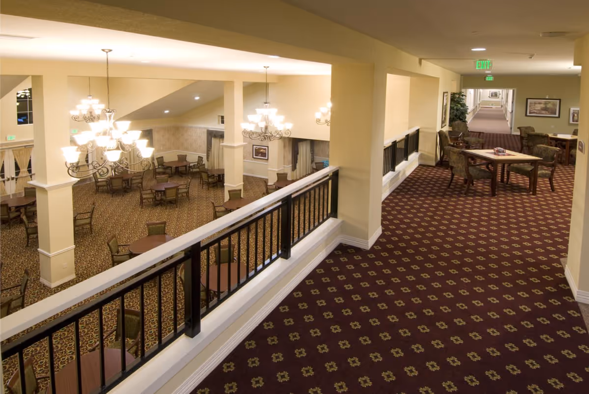 Second-floor interior hallway overlooking a large dining/lounge area with chandeliers, round tables, and patterned carpet.