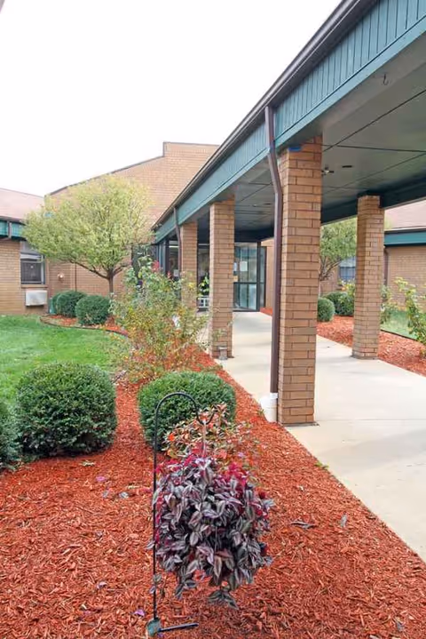 Brick building with a covered walkway and landscaped garden along a sidewalk.