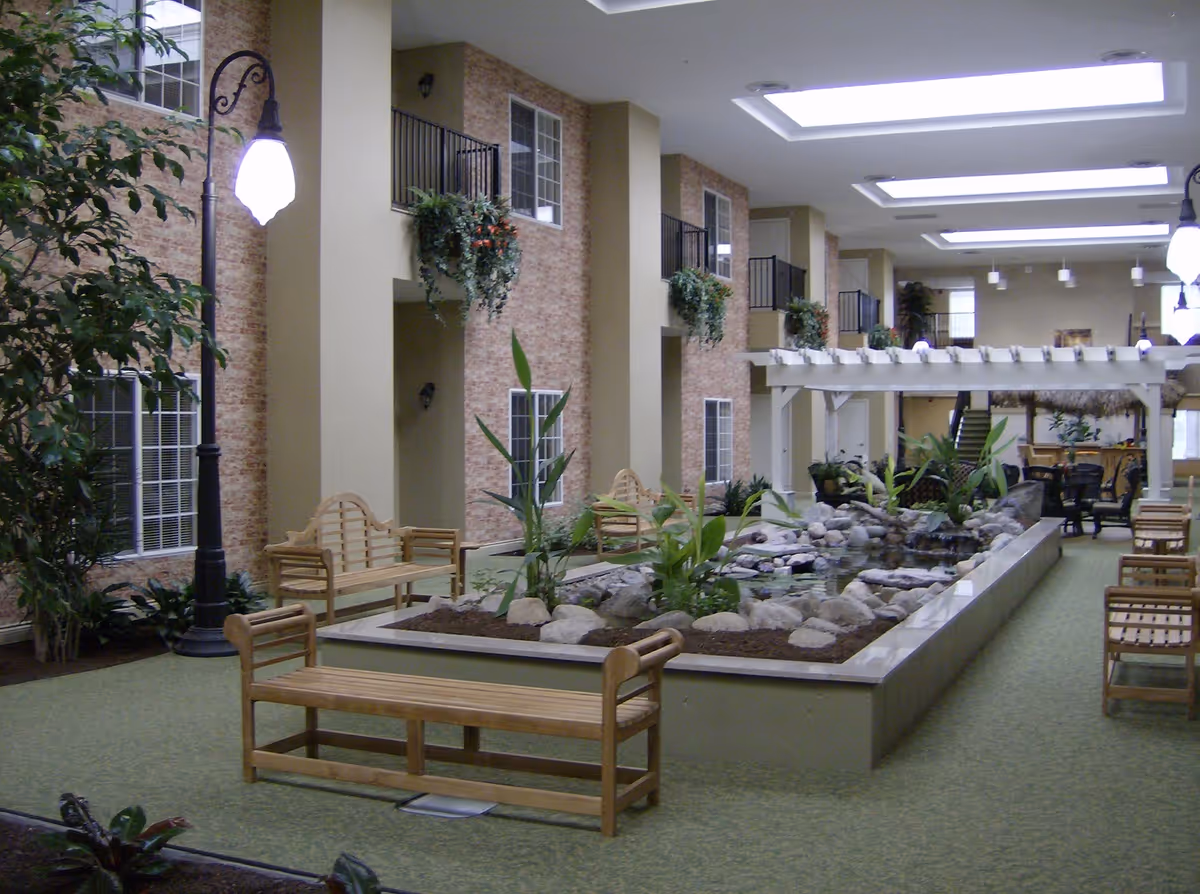 Indoor atrium-style common area with benches, plants, a central rock-lined water feature and skylights.