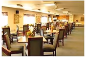 Spacious communal dining room with rows of tables and chairs and soft overhead lighting in a senior living facility.