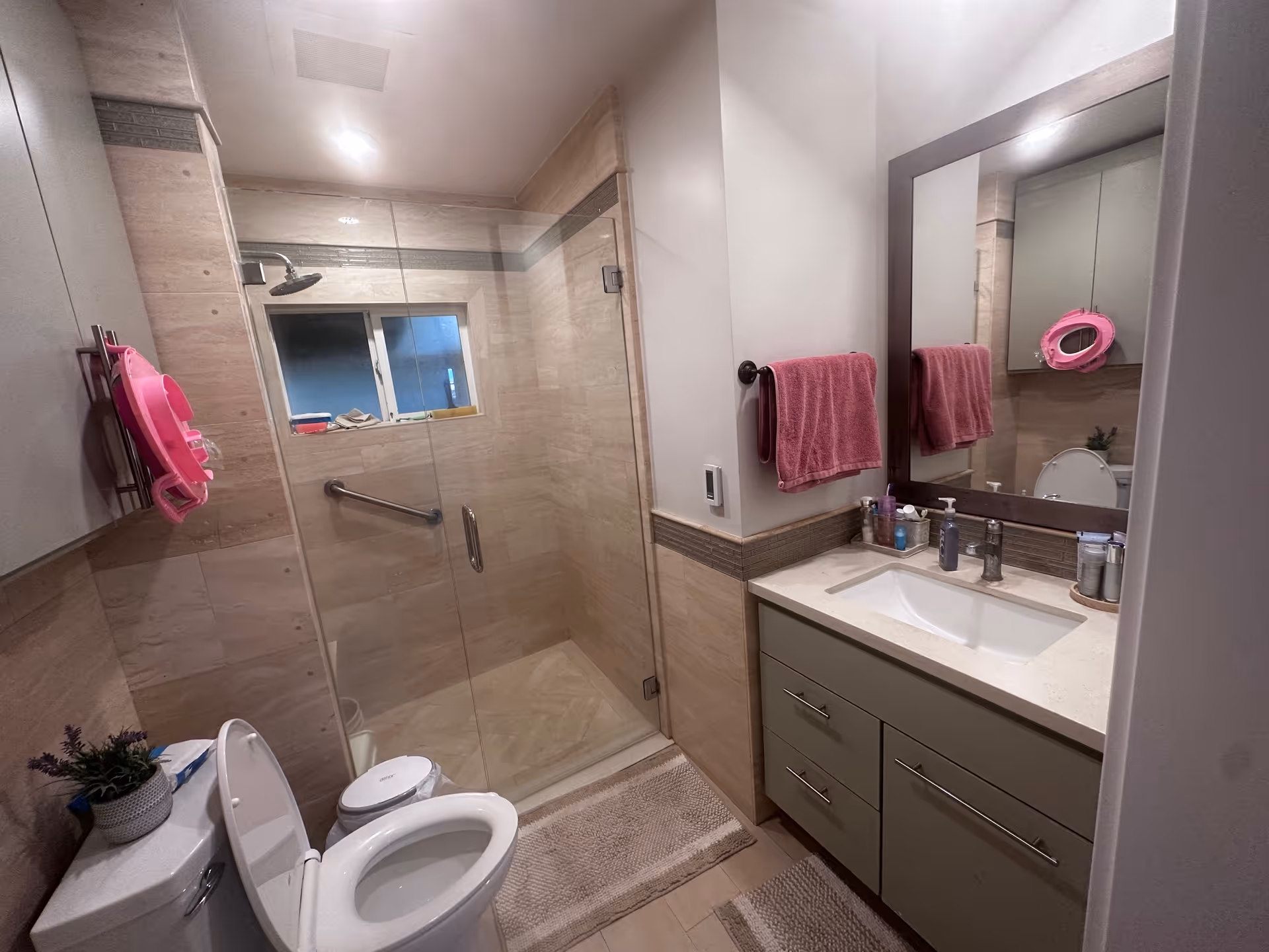 Modern bathroom with glass shower, double vanity, toilet, and pink towels.