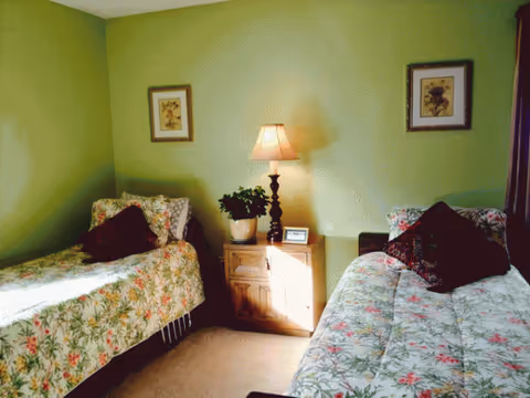 Two twin beds with floral quilts flank a wooden nightstand and lamp in a green bedroom.