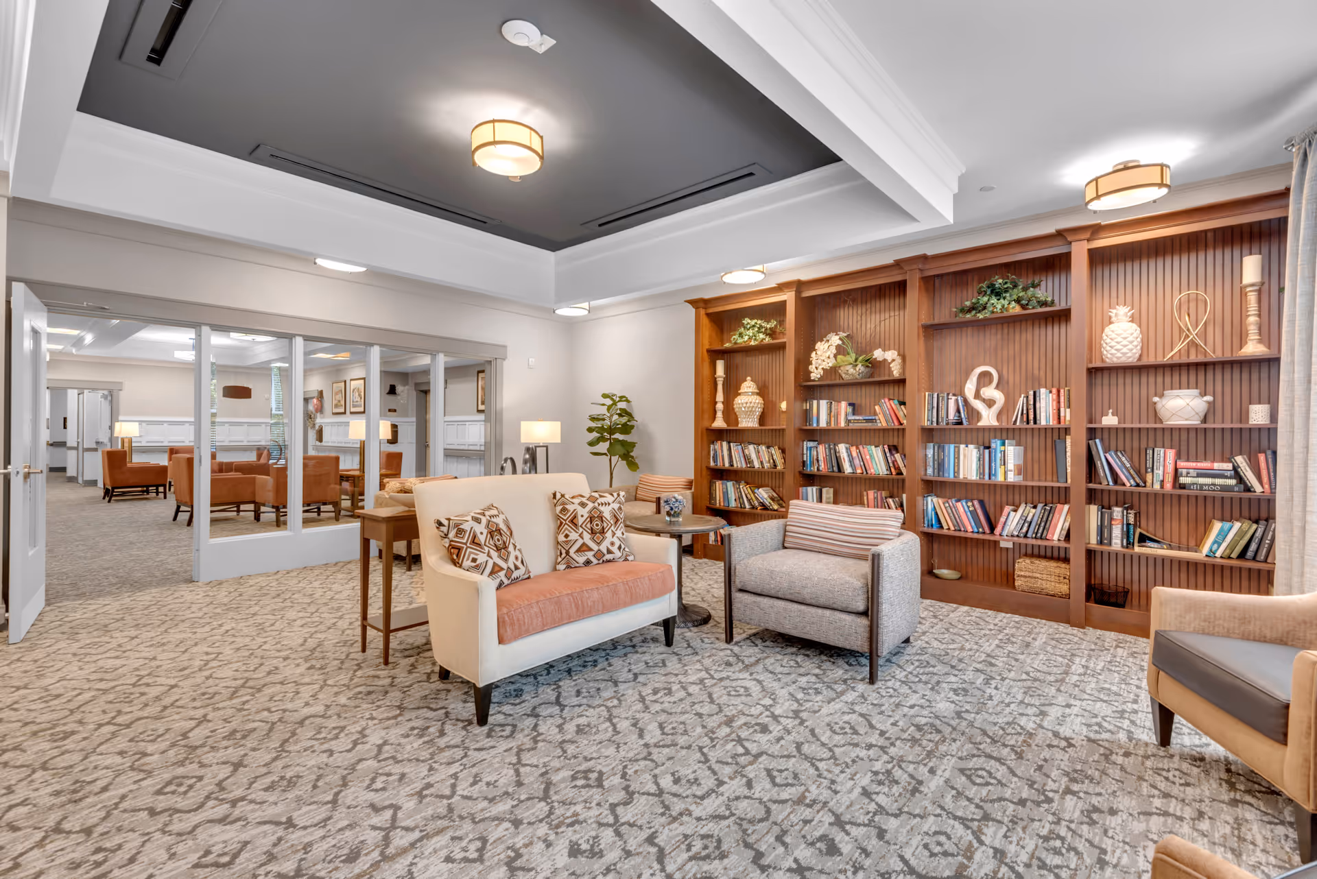 Cozy lounge area with armchairs, a loveseat, and built-in wooden bookshelves in a senior living facility.