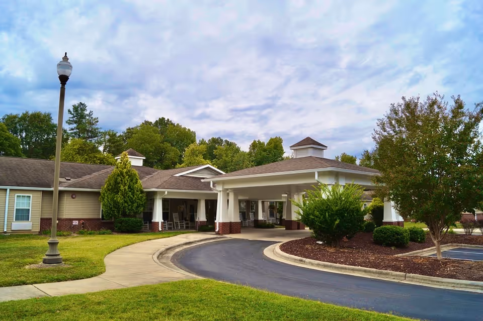 Front entrance and porte-cochère of a single-story senior living facility with landscaped grounds and a curved driveway.