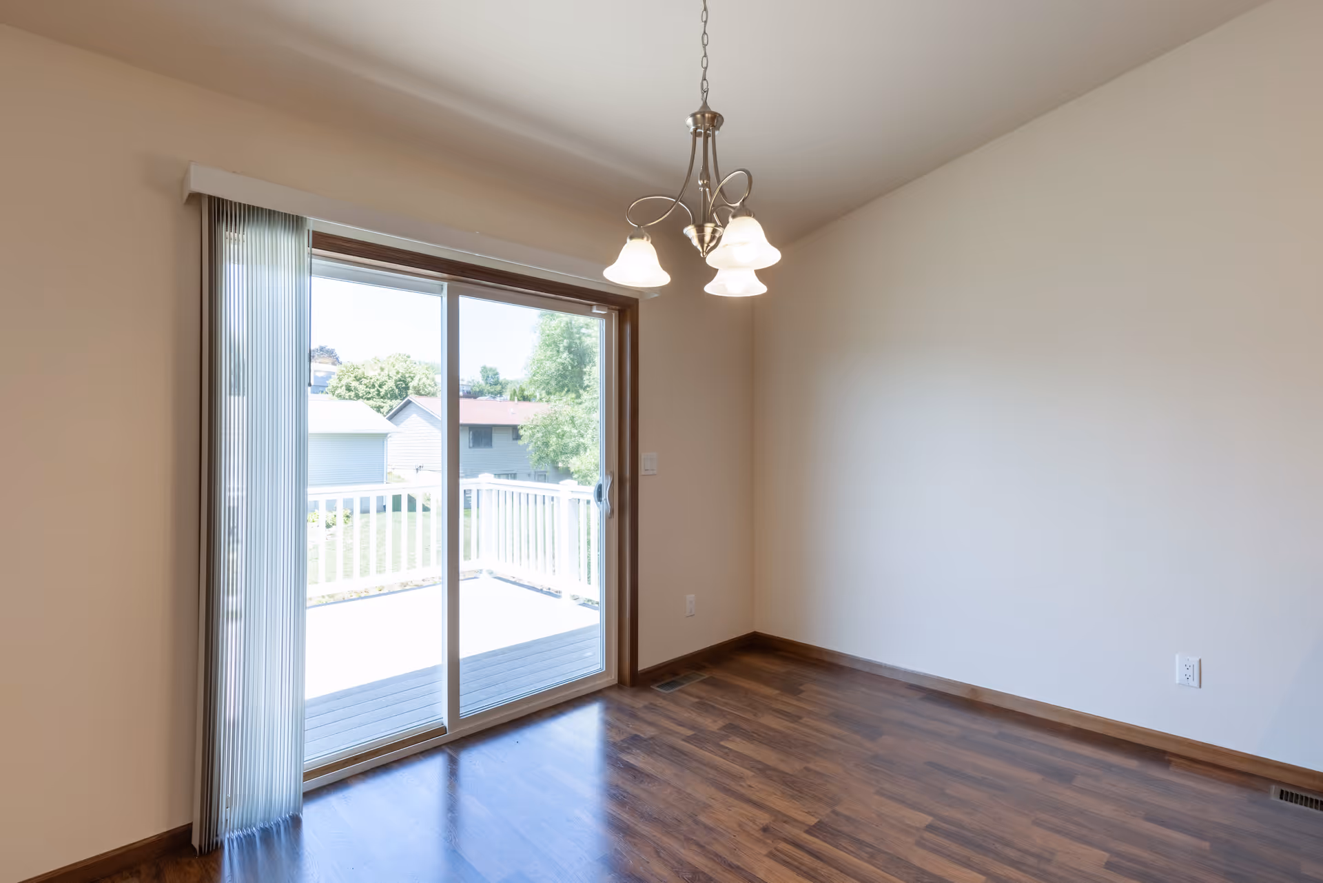 Empty dining area with hardwood floors, a hanging light fixture, and a sliding glass door opening to a deck.