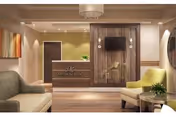 A modern and welcoming reception area in Meadow Park Rehab & Healthcare featuring a wooden reception desk with the facility's logo, a wall-mounted TV, comfortable seating including a green armchair and a beige sofa, a small round table with a plant, and warm lighting with a chandelier and recessed ceiling lights.