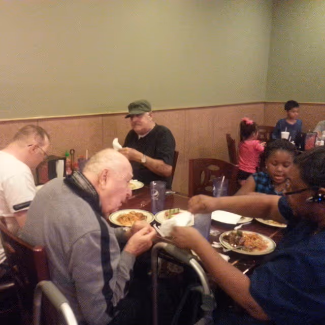 A group of elderly people and children sitting around a dining table eating a meal together in a casual dining room setting.