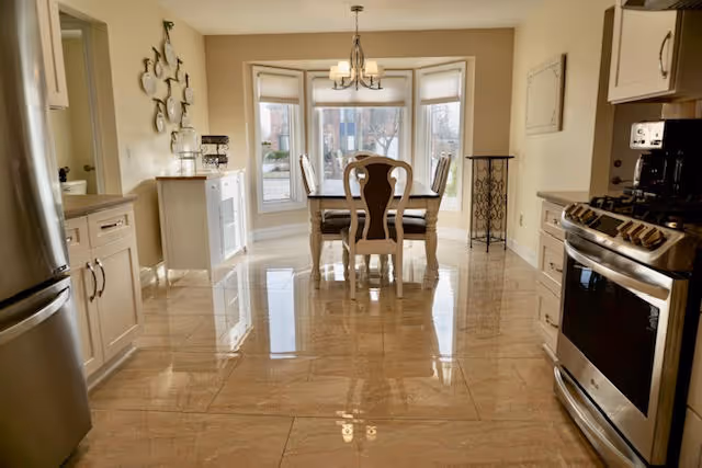 Bright kitchen with stainless steel appliances, cream cabinets, and a dining table by a bay window.