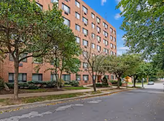 Brick, multi-story apartment building with trees lining the sidewalk.