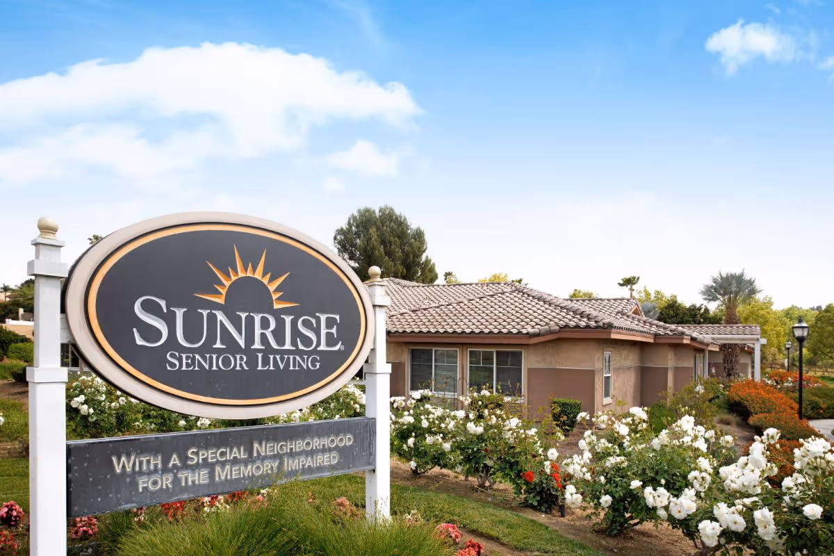 Large Sunrise Senior Living sign stands in front of a single-story building with a tiled roof and landscaped flowerbeds.