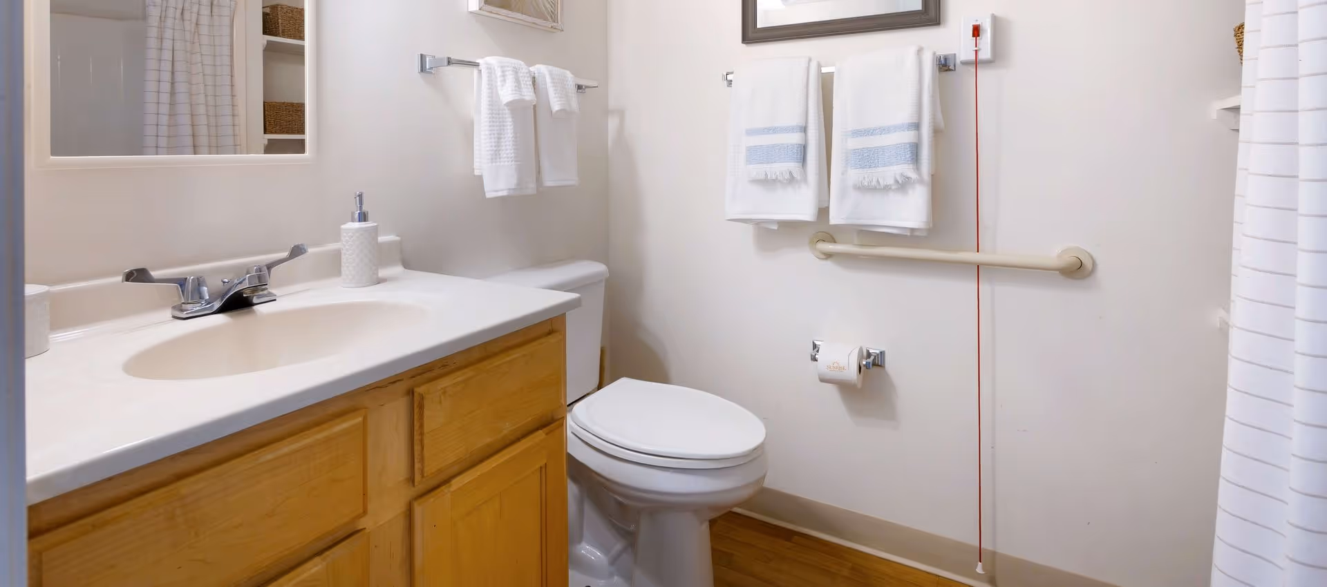 Clean accessible bathroom with a sink and vanity, toilet, grab bar, towel racks, and a shower curtain.