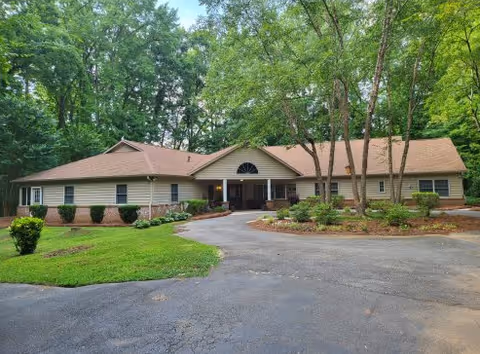 A single-story beige senior care facility fronted by trees and a curved driveway.