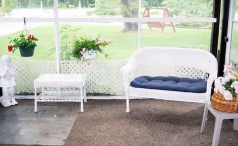 White wicker seating area with a blue-cushioned bench beside potted plants by a sunlit window.