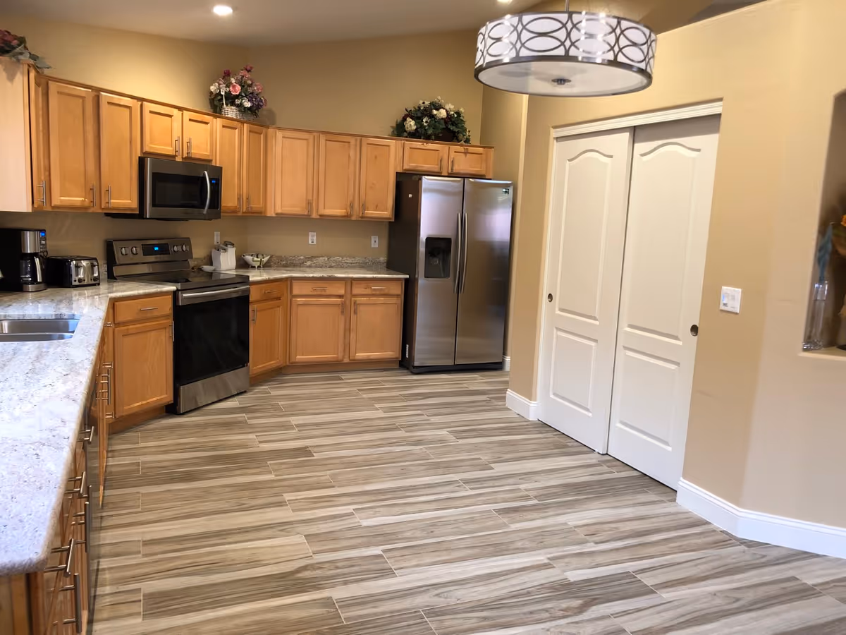 Spacious kitchen with light wood cabinets, stainless steel appliances, granite countertops and wood-look tile flooring.