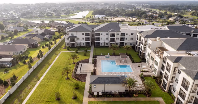 Aerial view of a senior living complex with three-story buildings surrounding a central courtyard featuring a swimming pool and landscaped lawns.