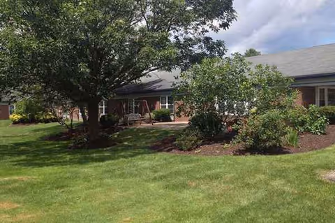 Front exterior of a single-story nursing home with a manicured lawn and trees.