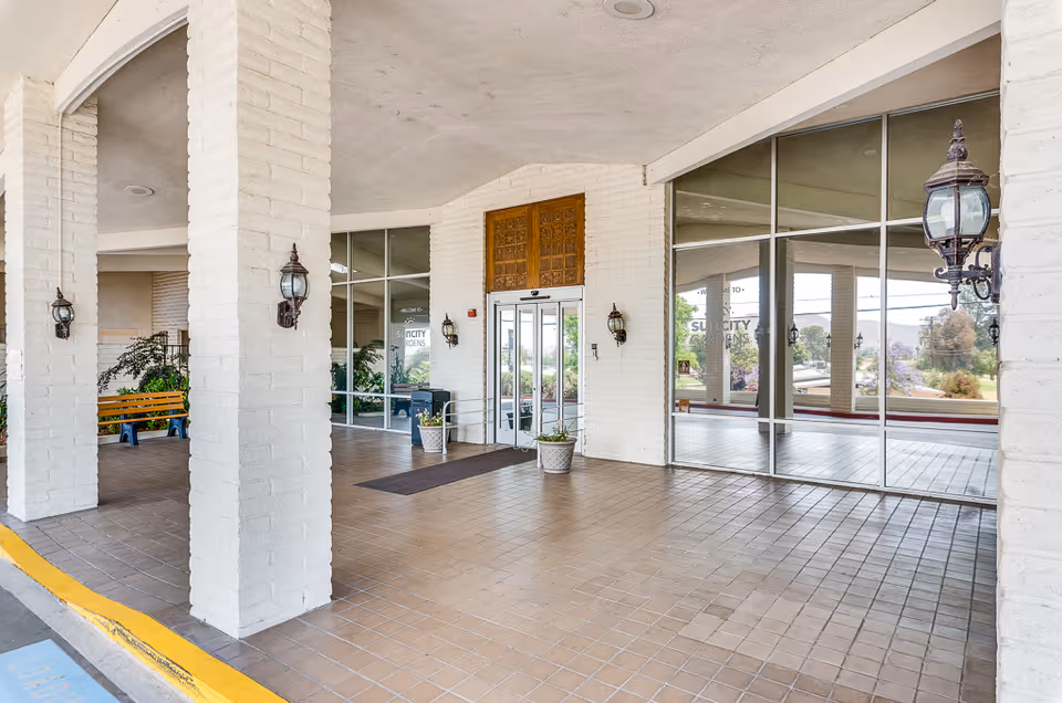 Covered entrance with white brick columns, tiled floor, glass doors, planters and lanterns at the Sun City Gardens building.