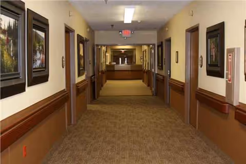 Long hallway in a senior living facility with doors, artwork, and a reception desk.