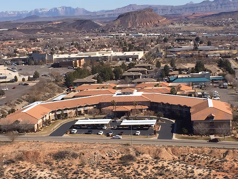 Aerial view of an assisted living complex with terracotta roofs in a desert town and mountains in the distance.