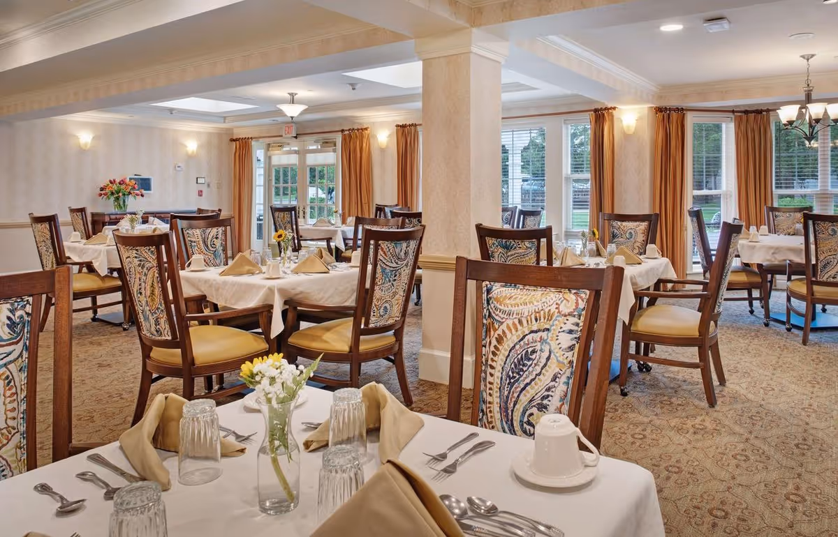 Bright, elegant dining room with multiple set tables and patterned chairs and large windows.