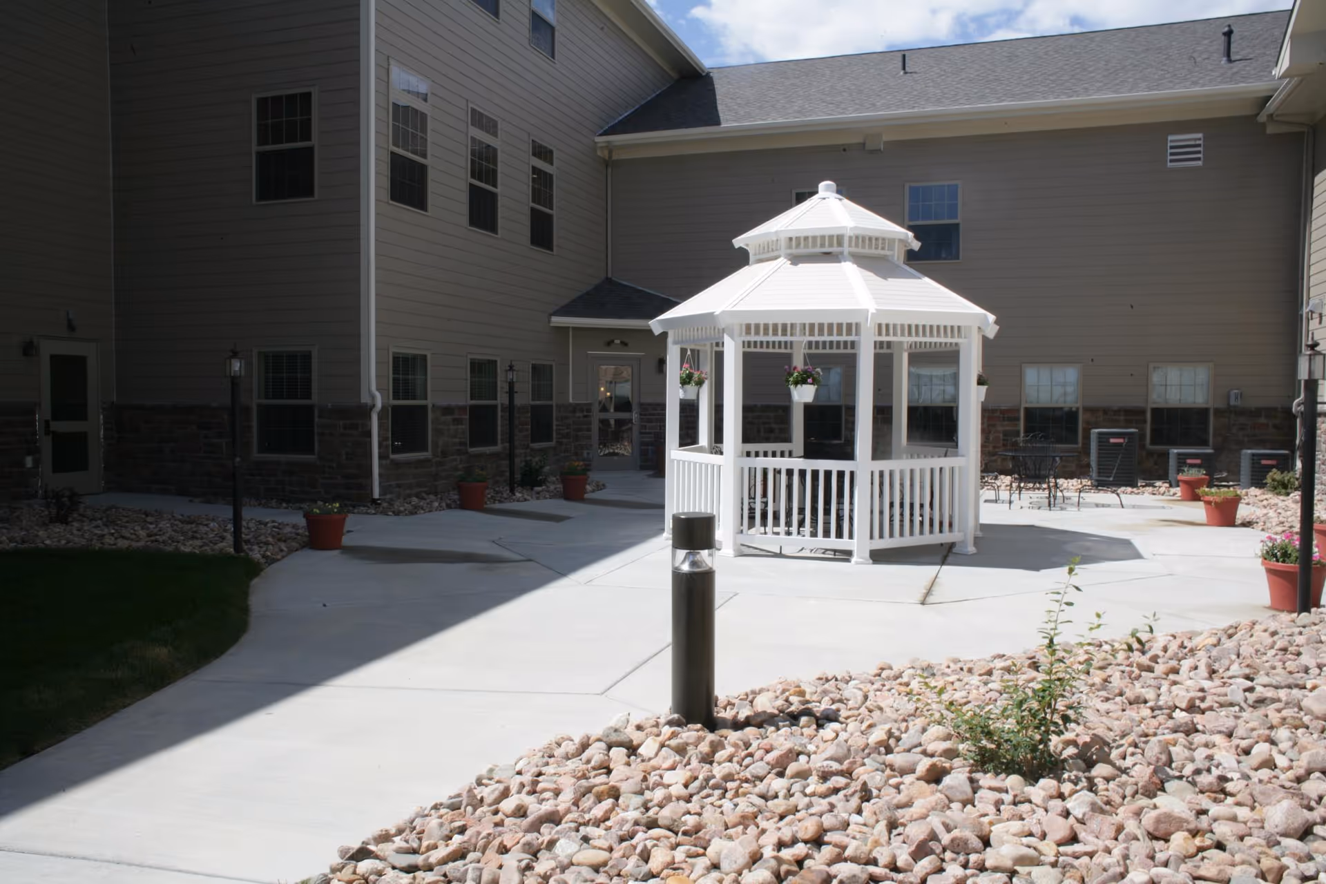 Courtyard of a retirement community featuring a white gazebo, concrete walkways, potted plants, and the surrounding building.