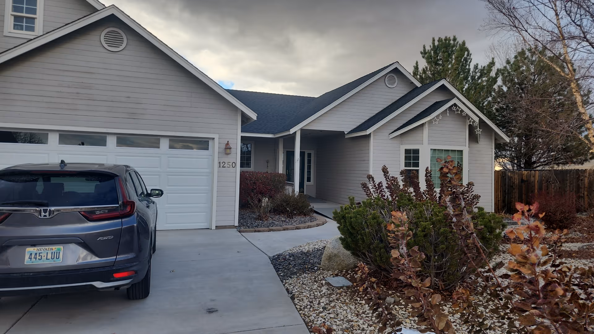 Front exterior of a single-story suburban house with a car parked in the driveway and a landscaped rock garden.