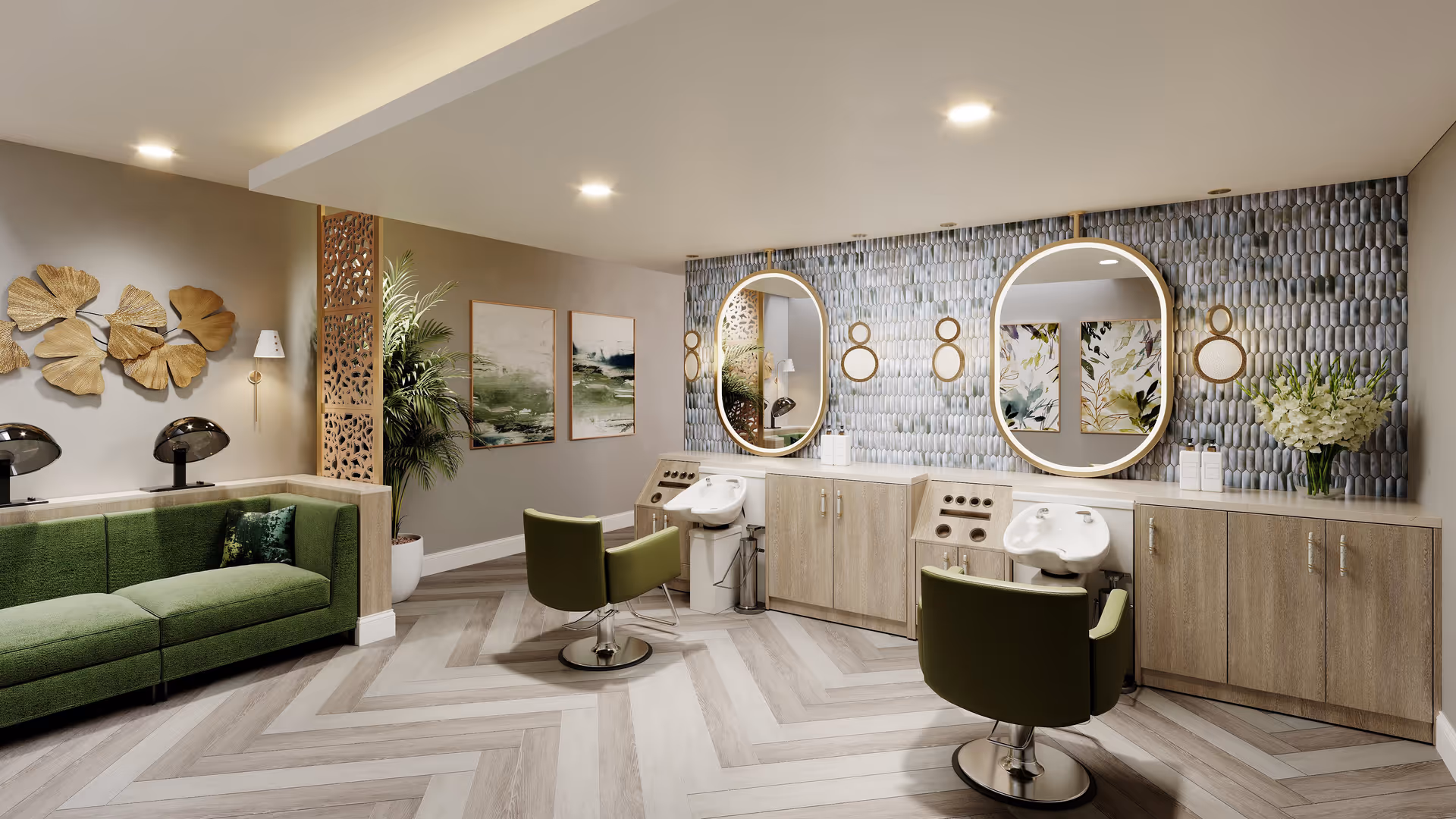 A modern salon area in a senior living facility featuring two green salon chairs in front of two wash basins and large oval mirrors mounted on a textured wall. To the left, there is a green upholstered sofa with two black hair dryers behind it, decorative gold wall art, and two framed paintings on the wall. The floor has a light wood herringbone pattern, and the space is well-lit with recessed ceiling lights.