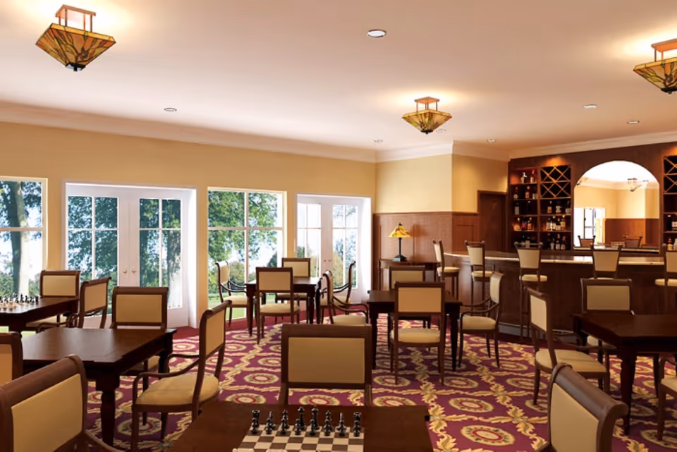 Spacious dining/lounge area with tables, chairs, a bar, and large windows overlooking trees.