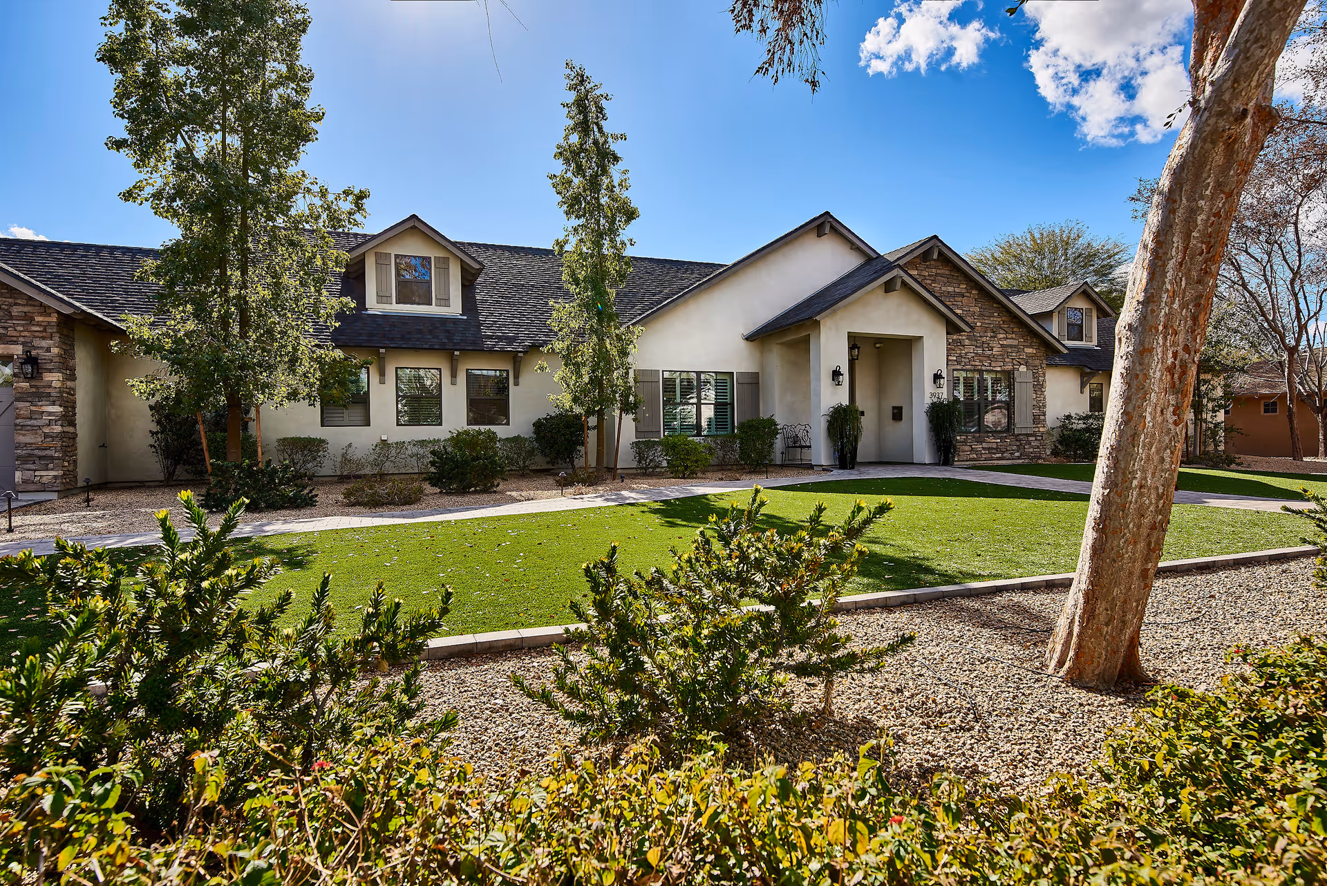 Exterior front view of a Paradise Living Centers senior living facility with a green lawn, trees, and a walkway.