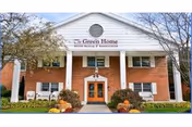 Front entrance of 'The Green Home' brick senior living building with white columns, a sign above the doorway and fall decorations.