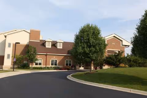 Exterior view of a brick senior living facility with a curved driveway, lawn, and trees.