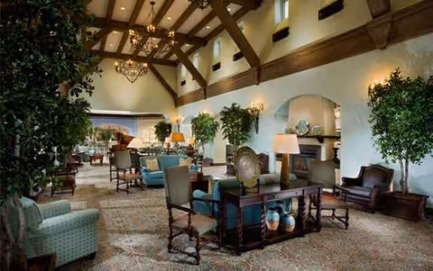Luxurious lounge with sofas, tables, lamps, plants, and a stone fireplace under timber beams.