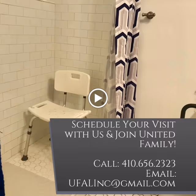A bathroom shower area with white tiled walls and floor, featuring a white shower chair and a blue and white patterned shower curtain.