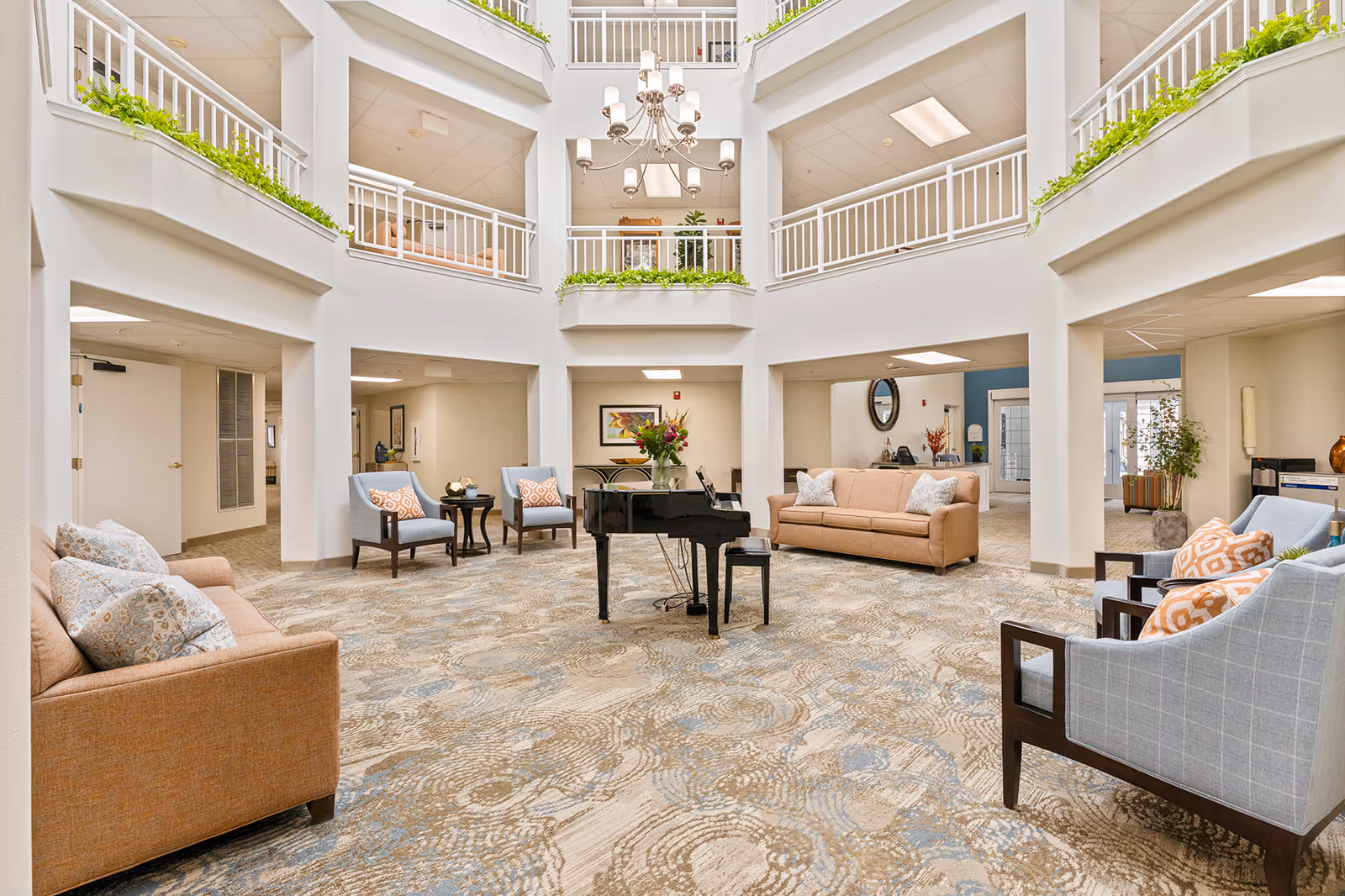 Spacious multi-level atrium lounge with sofas, chairs, a grand piano, balcony railings, a chandelier, and indoor plants.