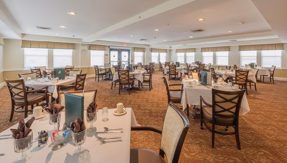 Bright, spacious dining room with multiple tables set with place settings and chairs.