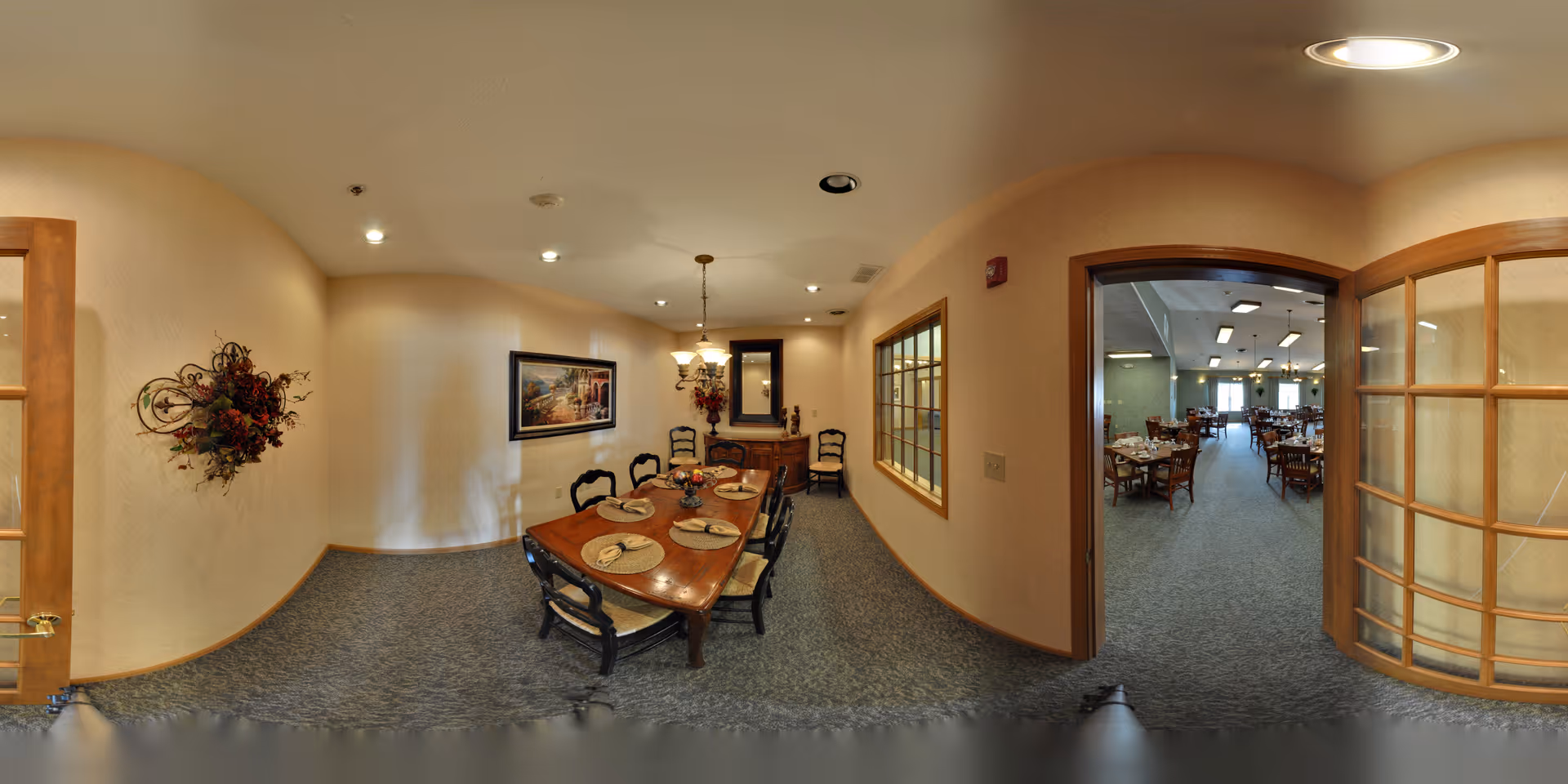 Small formal dining room with a set wooden table and chairs, decorative wall art, and an open doorway leading to a larger dining hall.