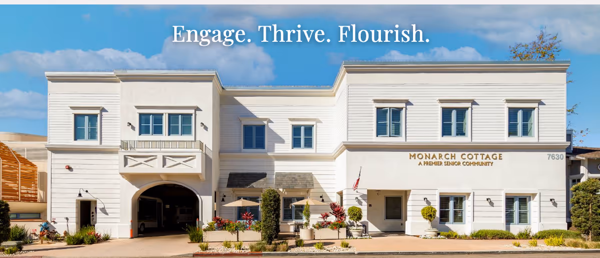Exterior front of the white two-story Monarch Cottage senior living building with landscaping, entrance, and the slogan 'Engage. Thrive. Flourish.' above.