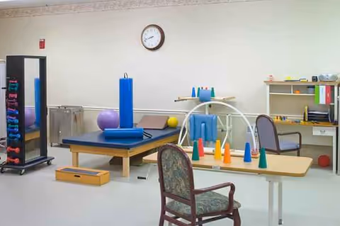 Interior therapy room with cones, balance equipment, mats, and chairs in a senior facility.