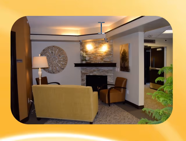 Cozy common-area living room with a sofa and chairs arranged around a stone fireplace.
