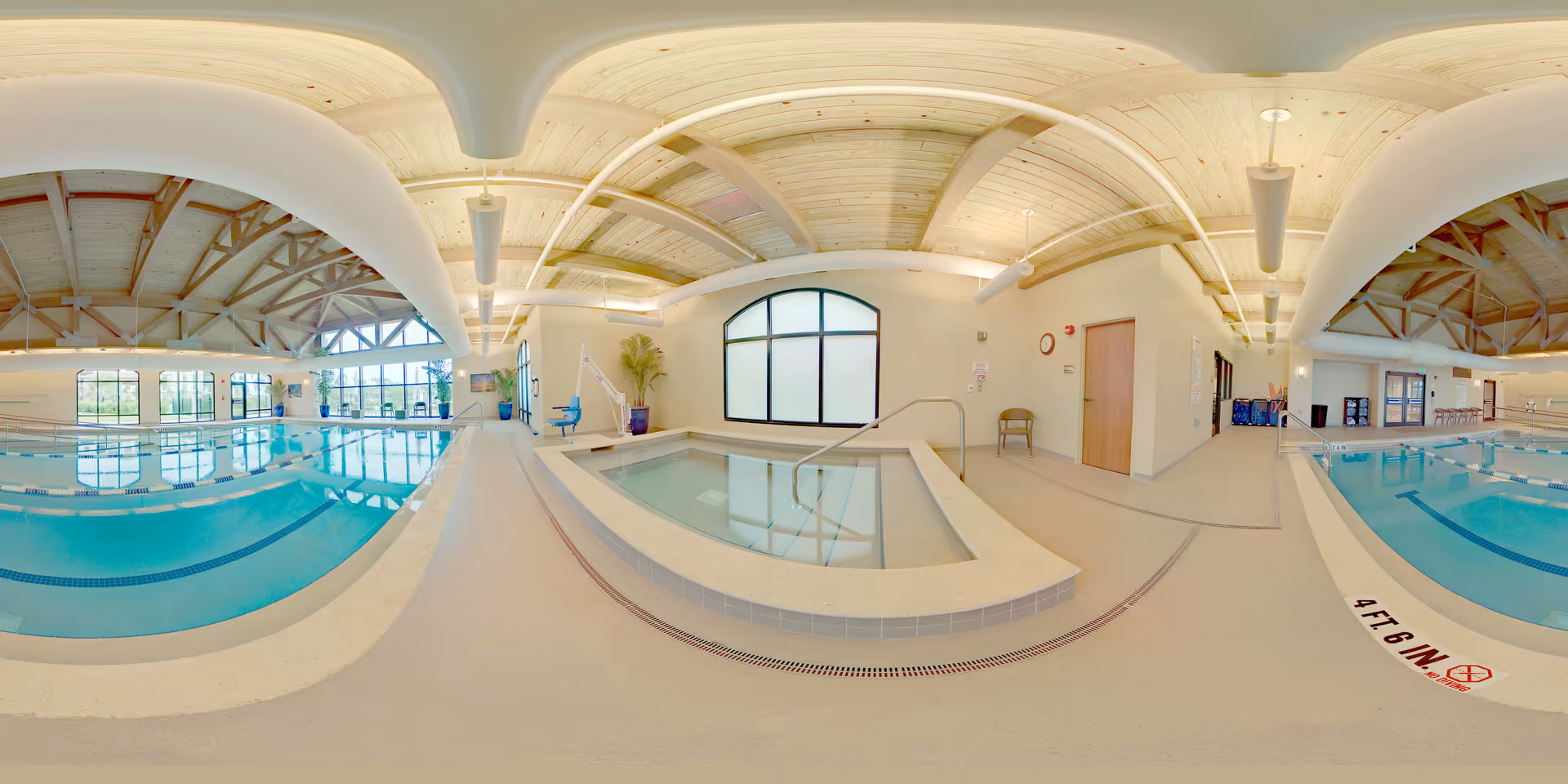 Indoor lap pool and adjacent hot tub in a bright recreation room with arched wooden ceilings and large windows.