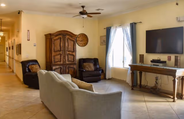 Sunny living room in a senior facility with a sofa, chairs, armoire, and TV.
