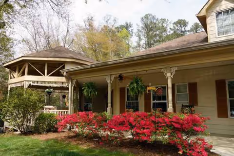 Front exterior of a beige senior living facility with a porch and red azaleas.