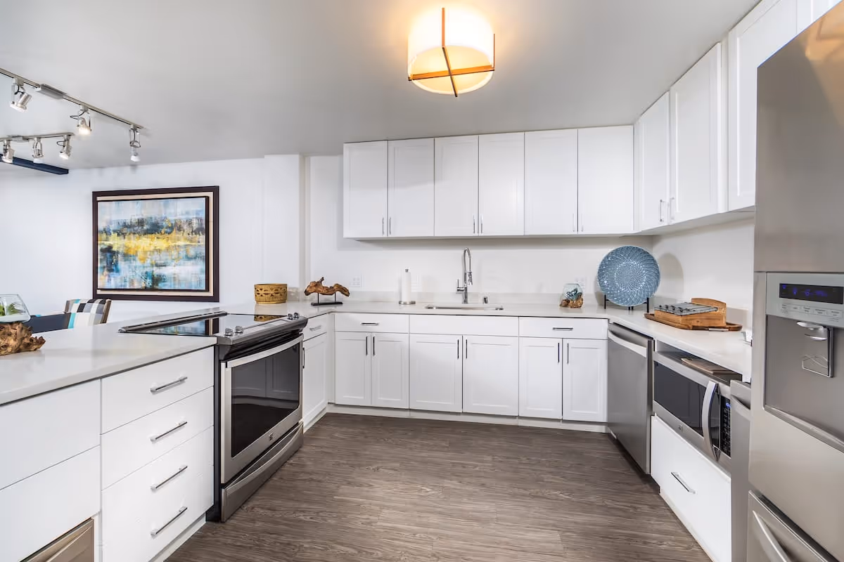 Modern white kitchen with stainless steel appliances, an island stove, white cabinets, and wood-look flooring.